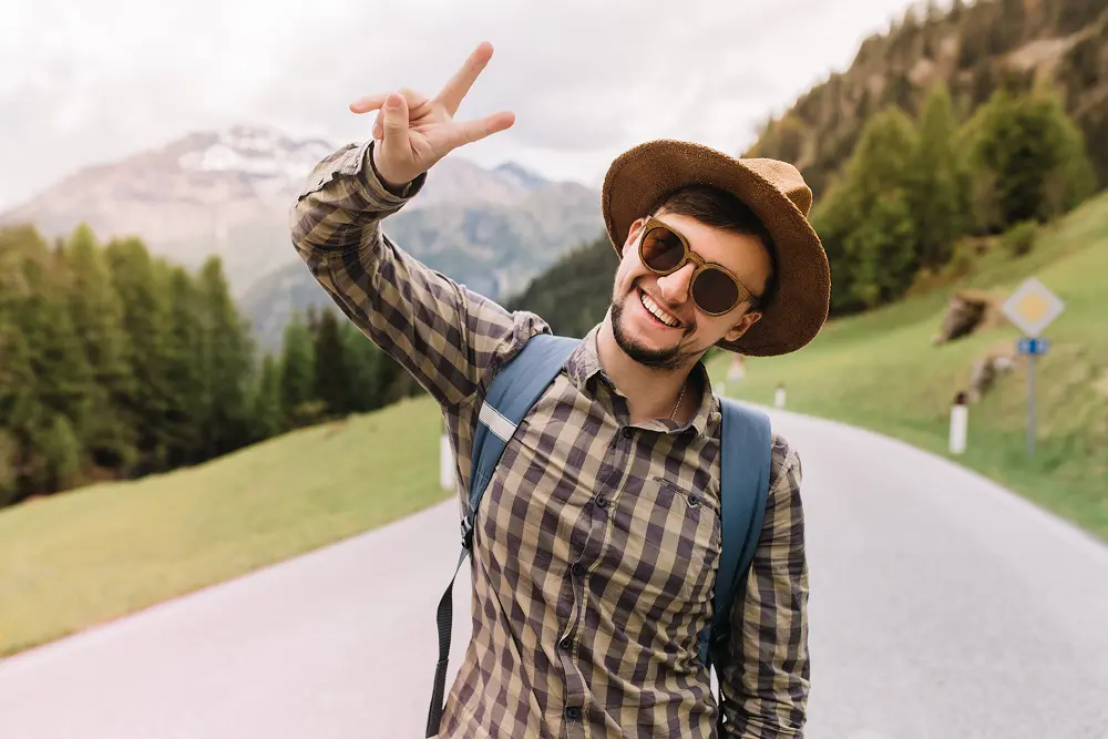 jovem-feliz-em-oculos-de-sol-da-moda-posando-com-um-sorriso-durante-uma-caminhada-nos-alpes-italianos-mostrando-o-simbolo-da-paz