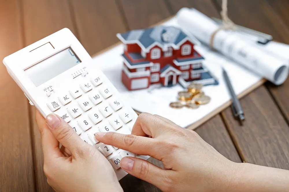 uma-mao-feminina-operando-uma-calculadora-na-frente-de-um-modelo-de-casa-de-villa 1